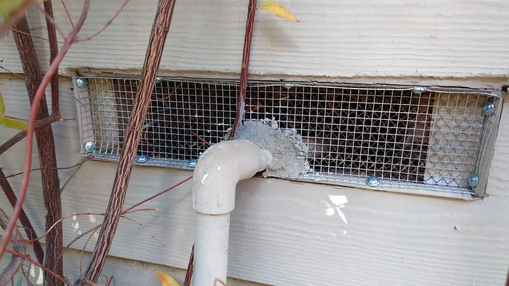 Foundation vent screened with metal mesh and a sealed pipe penetration on a Long Beach home